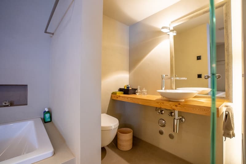 Bathroom with wooden vanity countertop, vessel sink, toilet, and shower area.