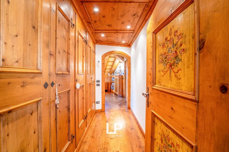 Wooden paneled hallway with arched doorway, floral artwork, and wooden floors