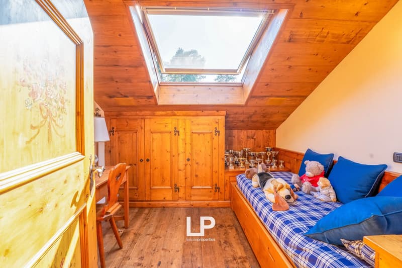 Cozy attic bedroom with wooden walls and ceiling, large skylight window, plaid bedding, stuffed animals, and wooden cabinets