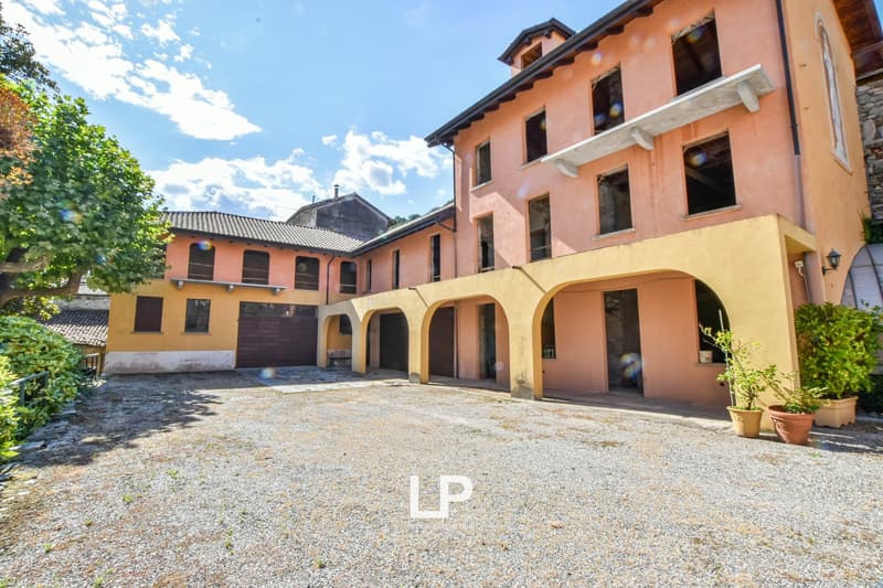 Multi-story building with a courtyard, arched entryways, and a gravel driveway. The building has a mix of orange and yellow exterior walls with tiled roofs.