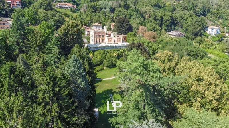 Large villa-style building with a terrace, surrounded by lush greenery and trees