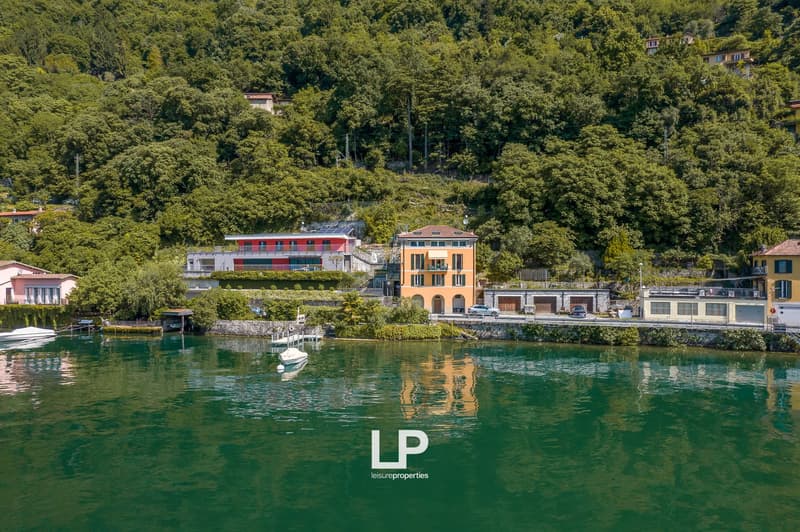 Lakeside houses with colorful facades, surrounded by lush greenery, with boats docked in the clear blue-green water