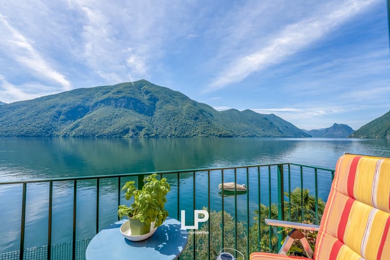 Balcony overlooking a scenic lake surrounded by mountains, with a potted plant and a colorful chair on the balcony