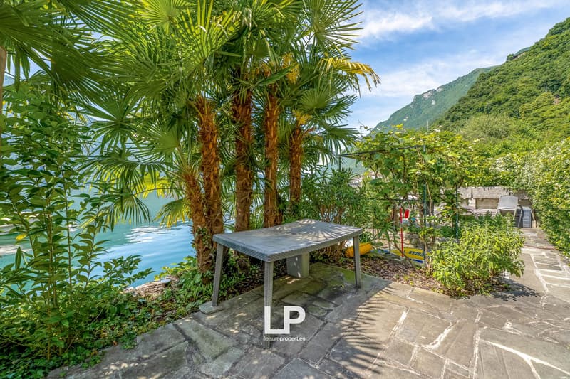 Lush tropical garden with palm trees, surrounded by mountains, outdoor table and chairs overlooking a body of water