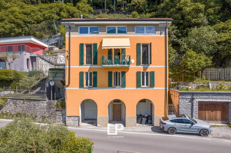 3 story yellow house, green shutters, archways, car parked in front, balcony with awning, carport entrance