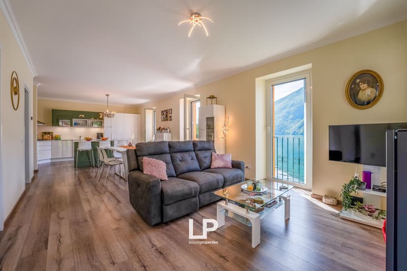 Open-concept living room and kitchen, hardwood floors, gray sofa, glass coffee table, balcony with scenic mountain view
