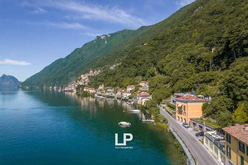 Scenic view of a lakeside town surrounded by lush green mountains, with colorful buildings, boats in the water, and a road along the shore