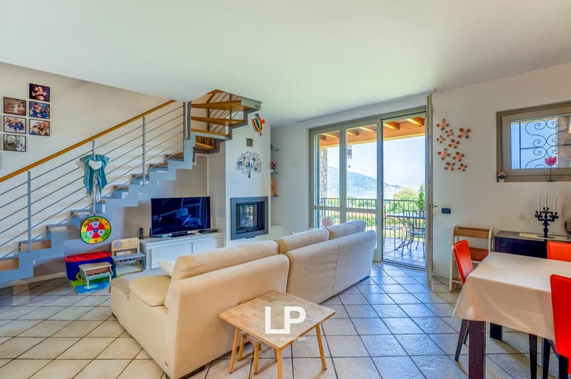 Open-concept living room with tiled flooring, beige sofa, fireplace, and access to a balcony or terrace with a view. The room also features decorative wall art, shelving, and a TV stand.