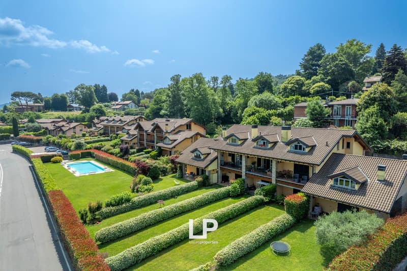 Multi-story apartment buildings with tiled roofs, surrounded by lush greenery, gardens, and a swimming pool in the center of the complex.