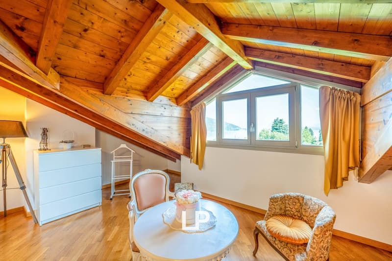 Cozy attic bedroom with wooden beamed ceiling, large windows offering a scenic view, wooden floors, dresser, and a small round table with chairs