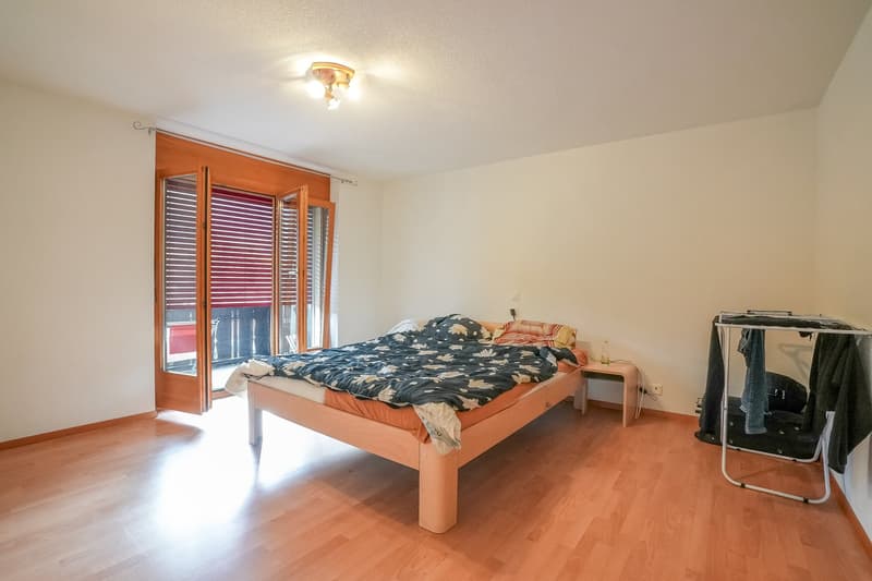 Spacious bedroom with hardwood flooring, large windows, wooden bed frame, and a balcony or terrace access