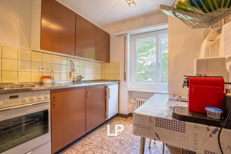 Spacious kitchen with wooden cabinets, tiled backsplash, stove, oven, and a window overlooking the outdoors. There is also a dishwasher and a private washing machine visible in the room.