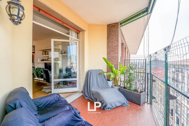 Balcony with brick walls, glass sliding door, lounge chairs, potted plants, and a view of the surrounding buildings.