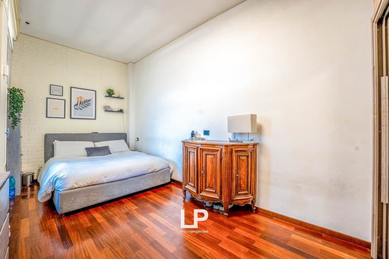 Spacious bedroom with hardwood floors, white walls, large bed with gray headboard, wooden dresser, and wall decor