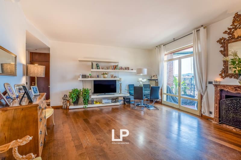 Spacious living room with hardwood floors, white walls, large windows, balcony, TV stand with shelves, blue chairs, and decorative items.