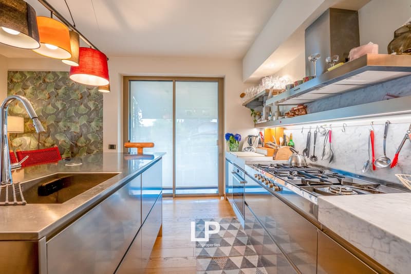 Modern kitchen with colorful pendant lights, marble countertops, gas stove, open shelving, and a sliding glass door leading to an outdoor area