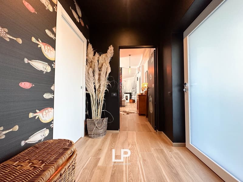 Hallway with dark walls featuring a fish print design, wooden flooring, a wicker basket, and dried floral decor. The hallway leads to a room visible in the background.