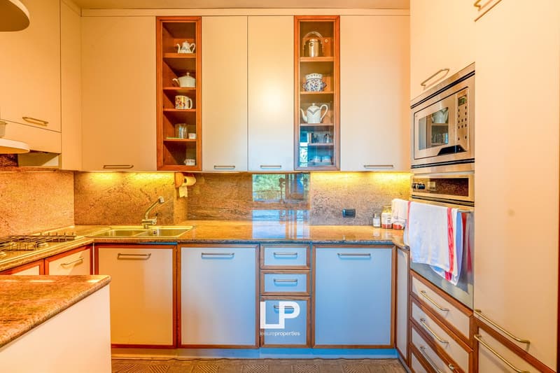 Spacious kitchen with granite countertops, wooden cabinets, built-in dishwasher, and private washing machine. The kitchen also features open shelving displaying decorative items.