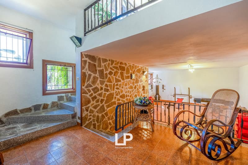 Stone wall, wooden staircase, rocking chairs, potted plants, tiled floor