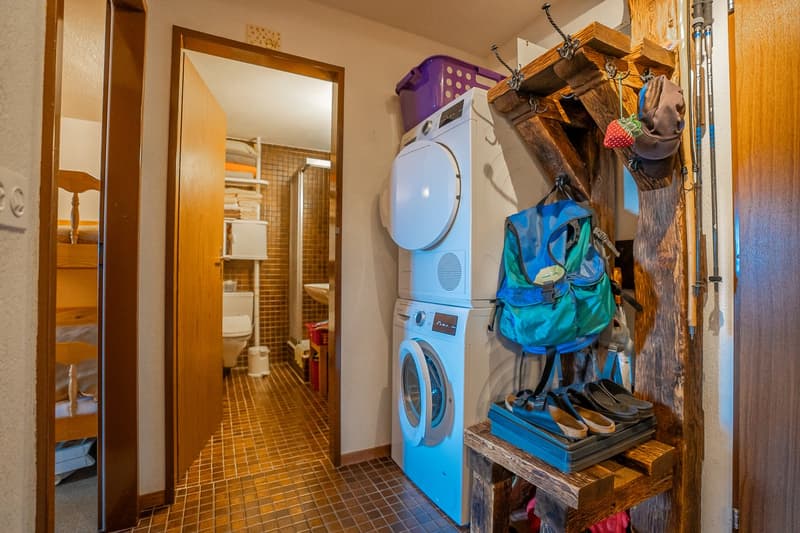 Laundry room with a washing machine and dryer, storage shelves, and a wooden bench with shoes and other items