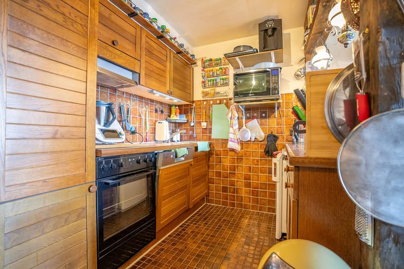 Wooden cabinets, tiled backsplash, oven, microwave, shelves with spices and cookware, washing machine, dishwasher