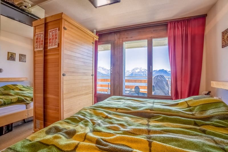 Spacious bedroom with wooden walls and furniture, large windows offering a scenic mountain view, and colorful bedding