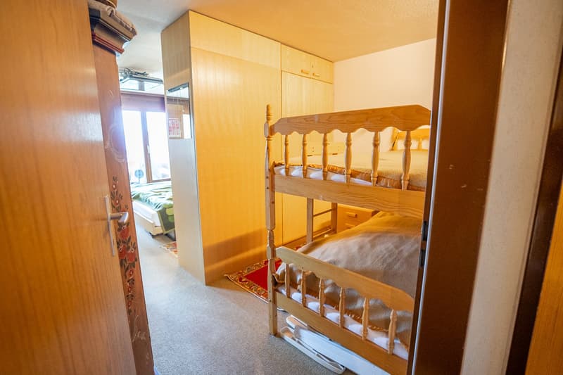 Wooden bunk beds, wooden wardrobe, carpeted floor, window with natural light