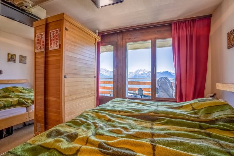 Cozy bedroom with wooden furniture, large windows overlooking snowy mountains, and colorful patterned bedding
