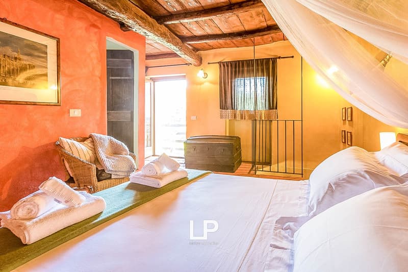 Rustic bedroom with wooden beamed ceiling, orange walls, large windows, wicker chair, trunk, and canopy bed