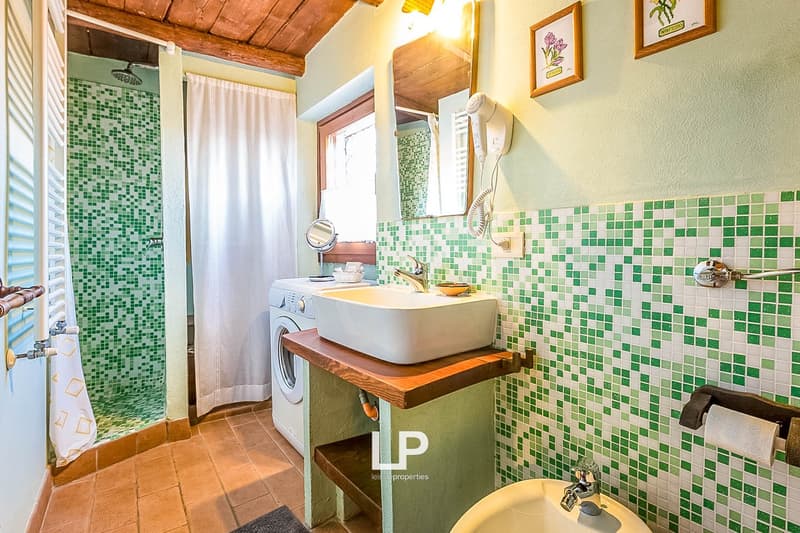 Rustic bathroom with green and white mosaic tile walls, wooden vanity with vessel sink, washing machine, and curtain-covered shower area