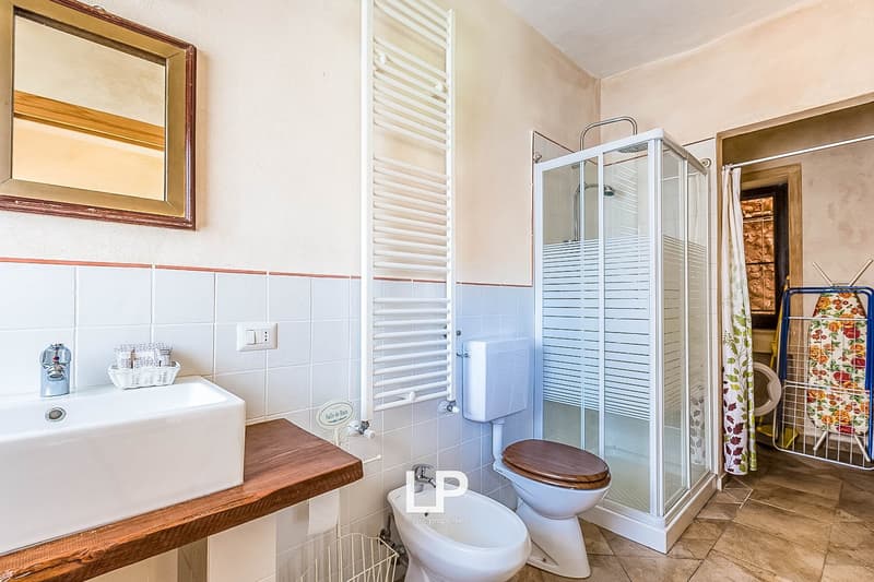 Tiled bathroom with a vanity sink, mirror, toilet, and glass-enclosed shower stall