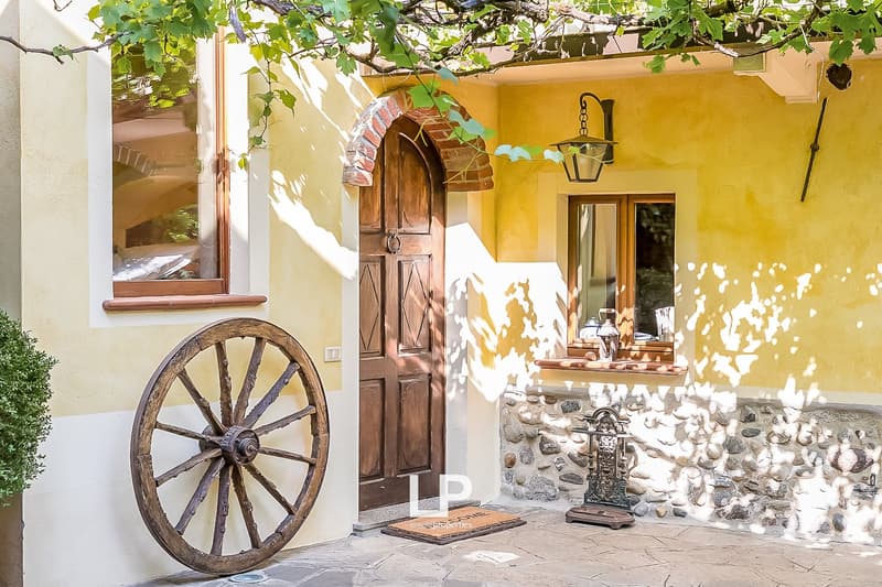Rustic wooden door with arched brick entryway, yellow exterior walls, wooden wagon wheel, decorative lantern, stone patio
