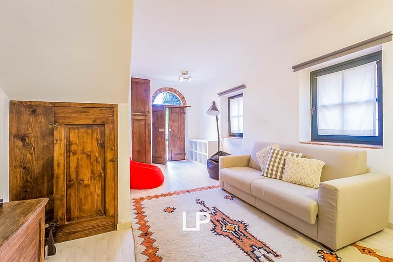 Spacious living room with wooden arched doorway, wooden furniture, beige sofa, patterned rug, and large window