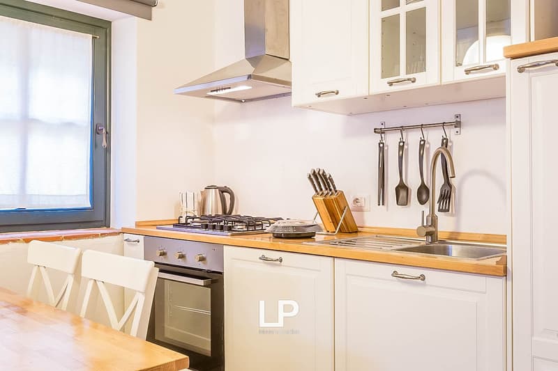 Modern kitchen with white cabinets, wooden countertops, gas stove, dishwasher, and kitchen utensils hanging on the wall
