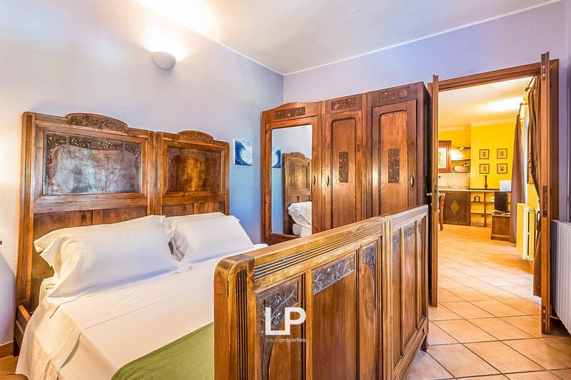 Spacious bedroom with ornate wooden furniture, including a large wardrobe and bed frame. The room has tiled flooring and a fireplace, creating a cozy and rustic atmosphere.