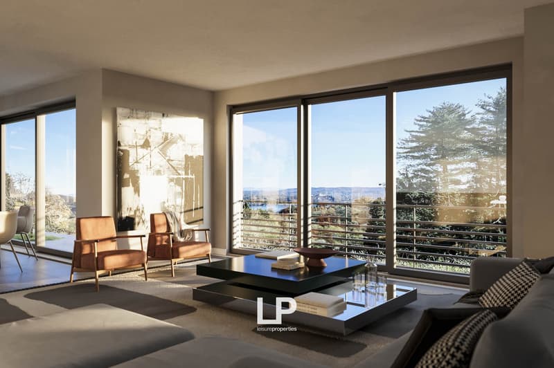 Spacious living room with large windows offering a scenic view of the surrounding landscape. The room features modern furniture, including a coffee table and armchairs, as well as a piece of artwork on the wall. The overall design has a minimalist and con