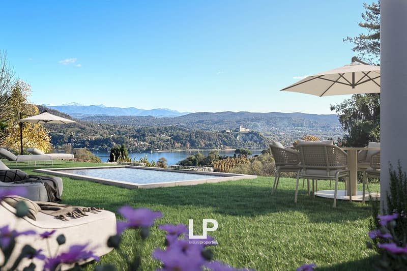 Luxury villa with outdoor pool, surrounded by lush green lawn and landscaping, with a scenic view of the mountains and lake in the distance. The property features patio furniture and umbrellas, providing a comfortable outdoor living space.