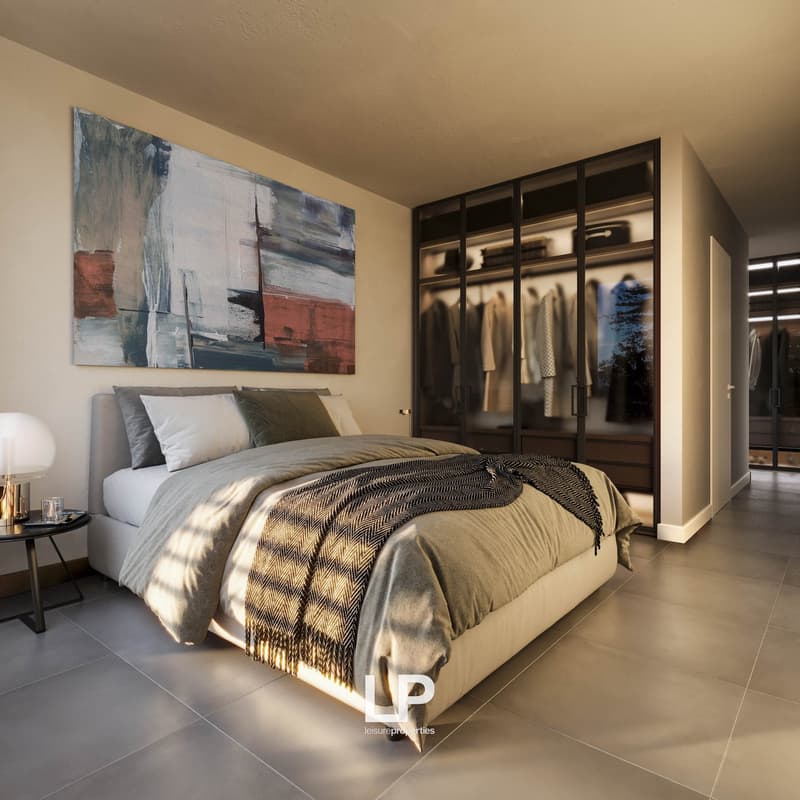 Spacious bedroom with a large abstract painting on the wall, a king-size bed with a patterned blanket, and a built-in wardrobe with glass panels. The room has a modern and cozy feel with the tile flooring and warm lighting.