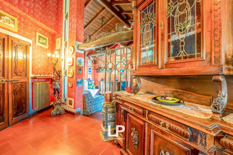 Red walls, terracotta floor, wooden cabinet with glass doors, radiator, ornate door, decorative pieces, table with bowl, radiator, fireplace, decorative plate, hanging lamp