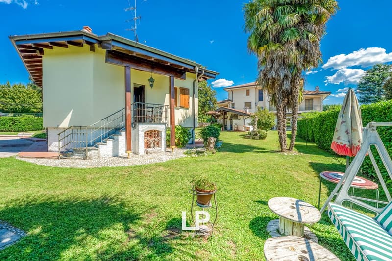Detached house, beige walls, metal railing, brick fireplace, balcony, lush lawn, palm tree, bench and table in the garden