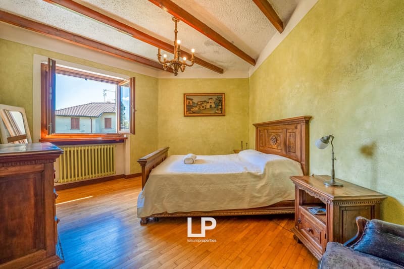 Large bed, wooden headboard, white bedspread, nightstand with lamp, wooden cabinet, mirror, radiator, picture frame on wall