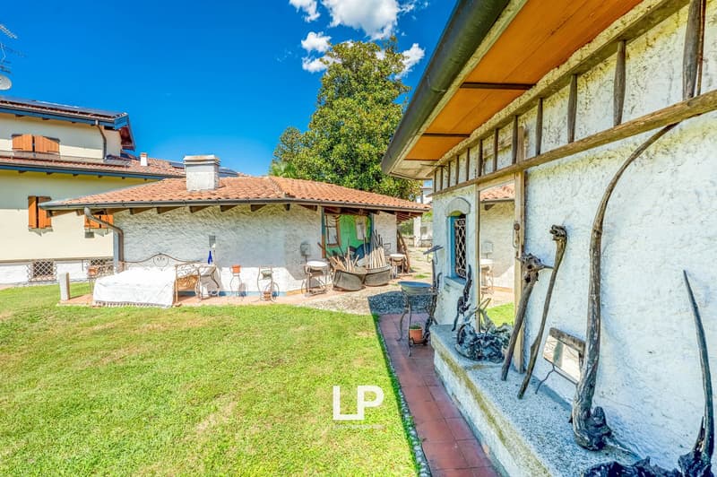 two buildings, one with brown roof, grassy yard, patio with daybed, brick walkway, objects on wall