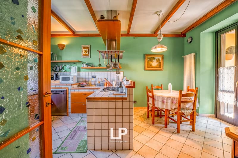 kitchen area with tile flooring, kitchen island with a gas stove, wooden dining table, green walls, picture frames, lamp, wall radiator, and entrance door