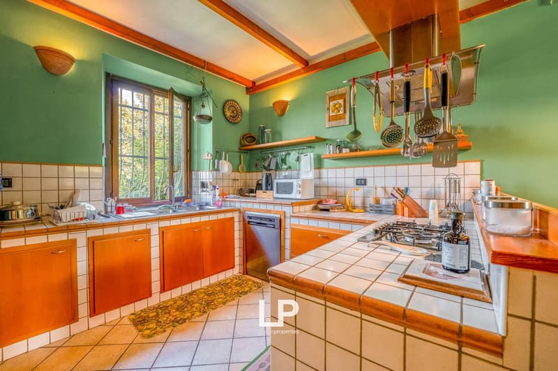 wood cabinets, green walls, tiled floor, open concept kitchen, gas stove, microwave, sink, utensils rack, natural light from window