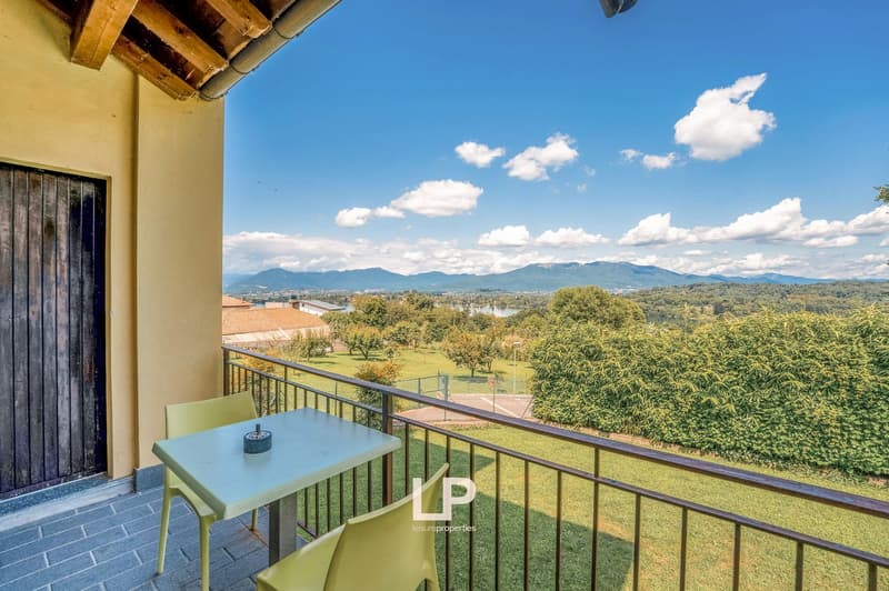 Terrace with wooden floor, wooden balcony railing, yellow chairs, square table, open landscape view, mountains in the distance