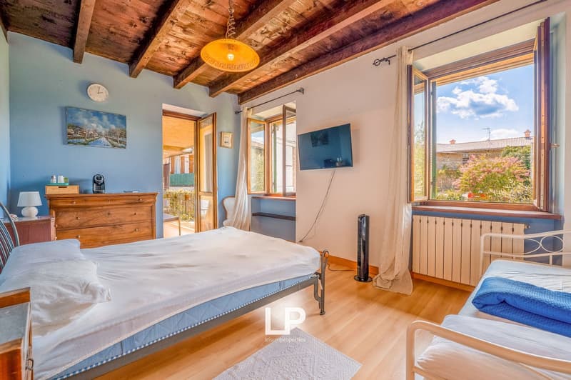 bedroom with two single beds, wooden floor, blue walls, wooden ceiling, radiator, tv, open window with balcony view, lamp, wooden dresser with coffee maker, clock, painting