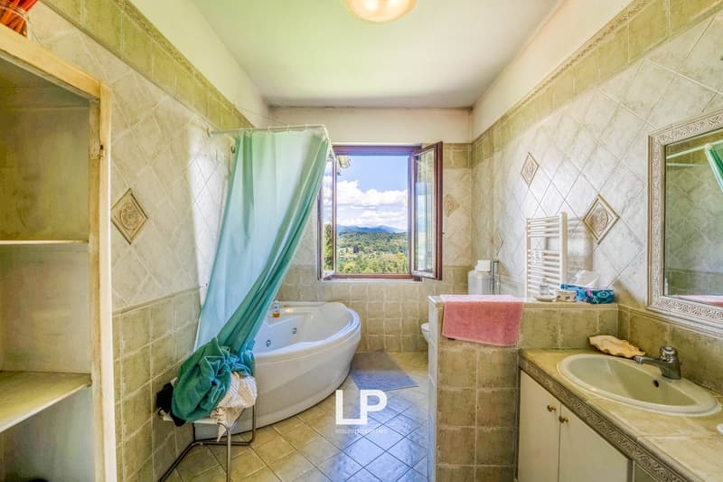 White bathtub, separate shower area, mirror, sink, window with landscape view, decorative tiles, wooden cabinet