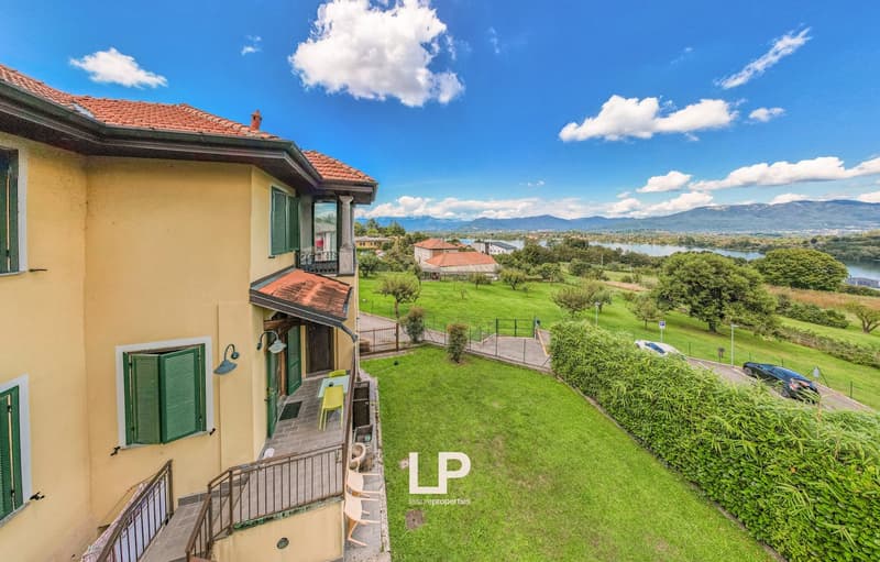 Detached house, red roof, yellow walls, green shutters, outdoor table, large lawn, trees, mountain and lake view