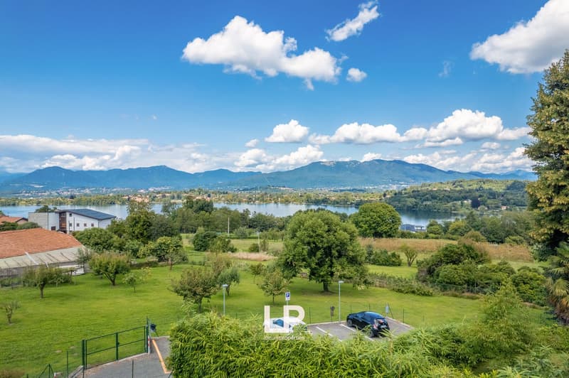 Parking area with lake view, parked car, trees and grass, mountain range in the distance