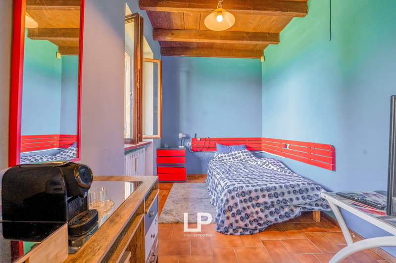 Bedroom with bed, bedside drawers, small desk, coffee machine, mirror, radiator, rug, and tiled floor.